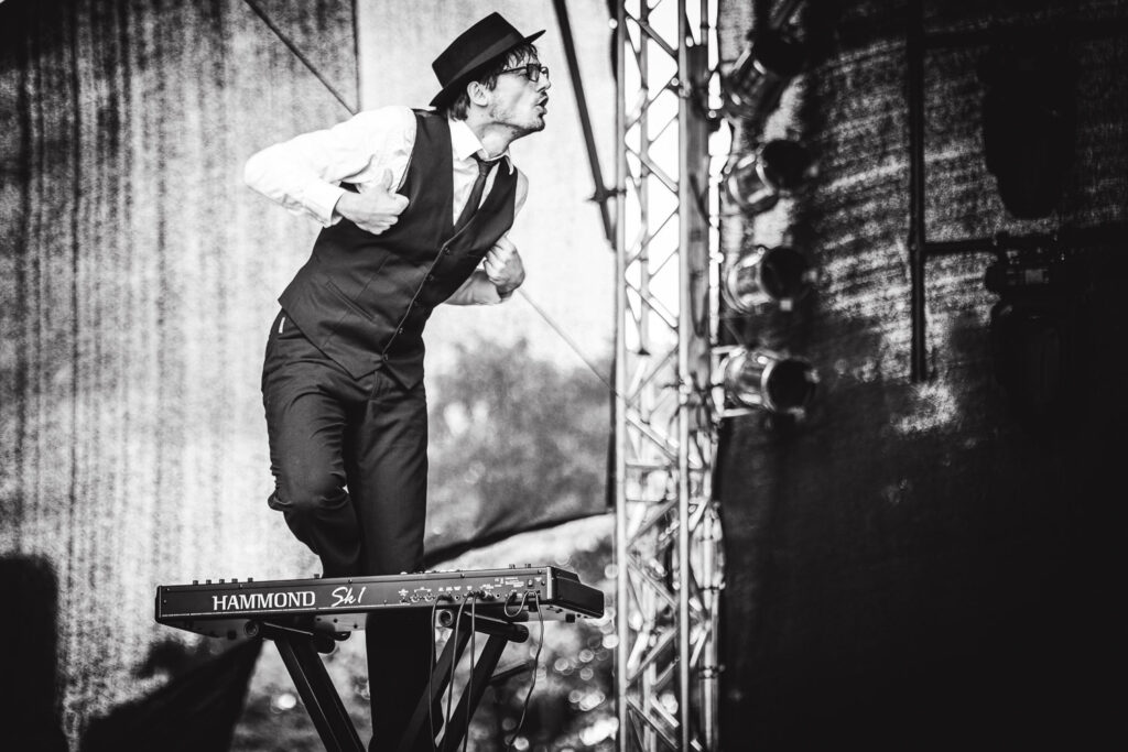 Konzertfotografie. Ein Mann steht lustig auf einem Keyboard.