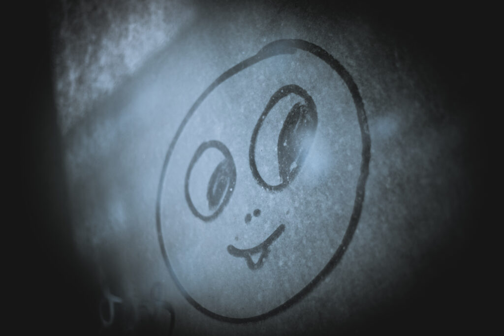 Ein lachendes Gesicht in den Staub eines Fensters gemalt